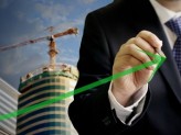 man in business suit holding up a green arrow with a building that is under construction in the background